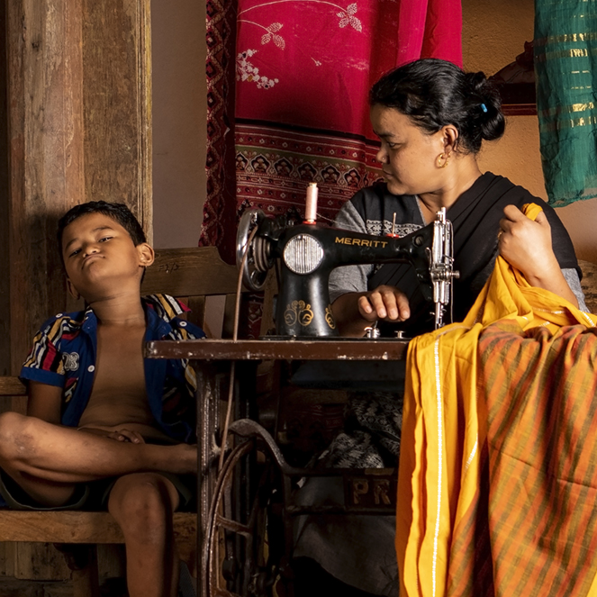 A Nepalese tailor frowns at her son while a shop-hand works on saris.