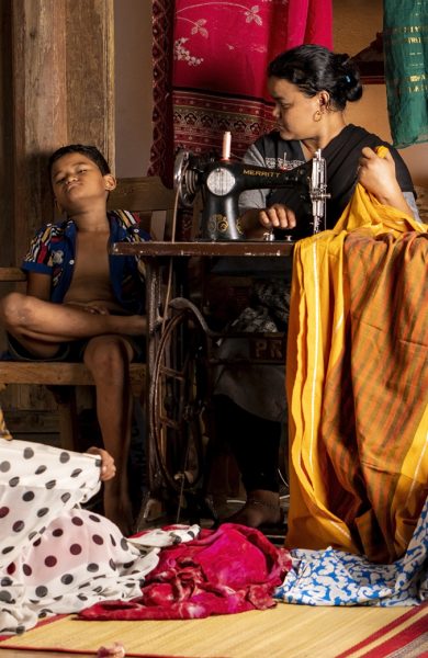 A Nepalese tailor frowns at her son while a shop-hand works on saris.